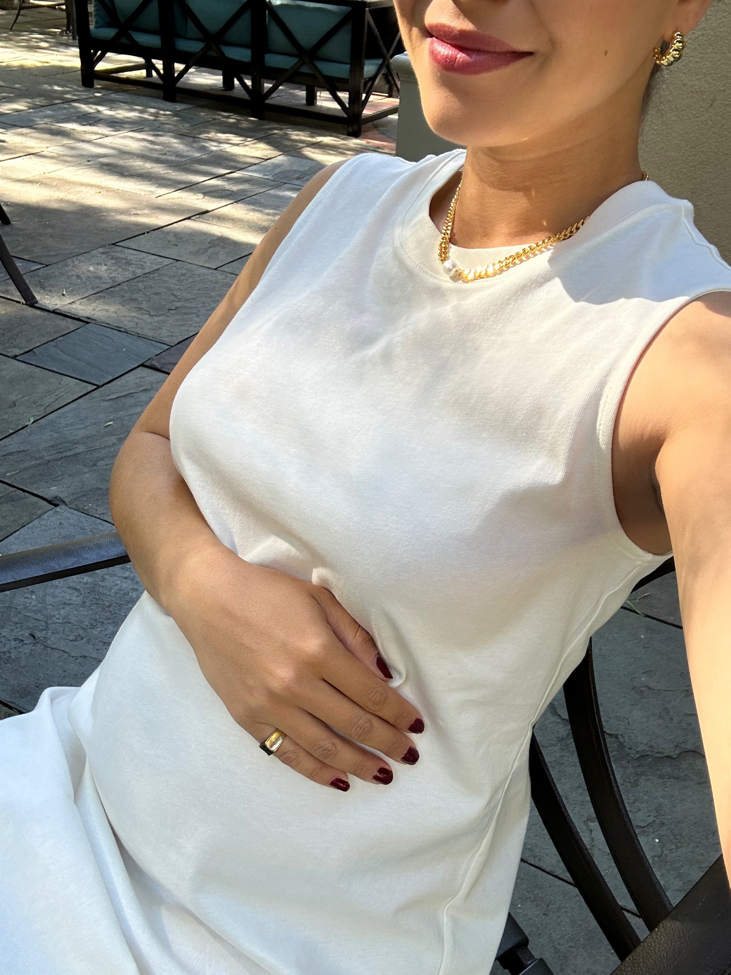An expecting mother models thick 18k gold plated fine jewelry including necklace and earrings glimmering on a summer terrace