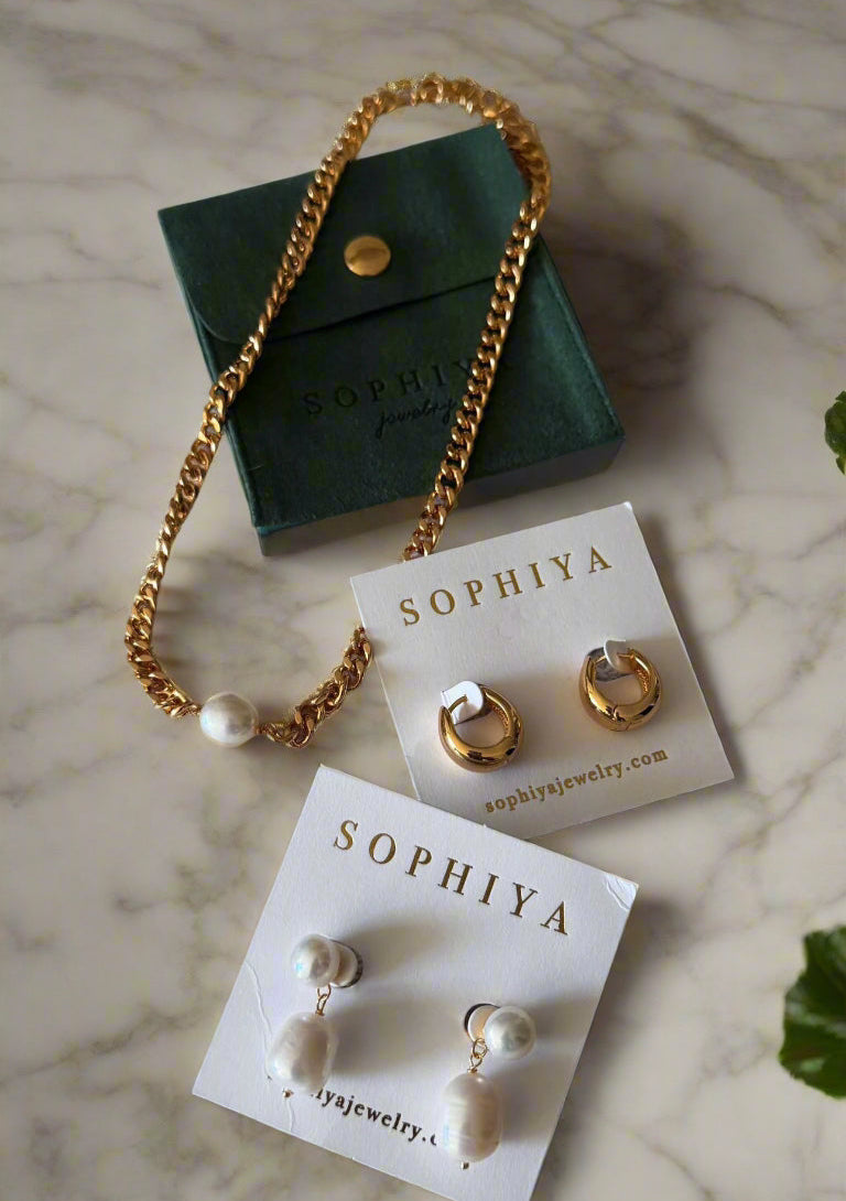 Jewelry spread on marble counter top - Dakota statement huggies, 18k gold hoop earrings, baroque pearl teardrop dangles, elegant classic evening looks, thick flat bevelled curb LIliana chain