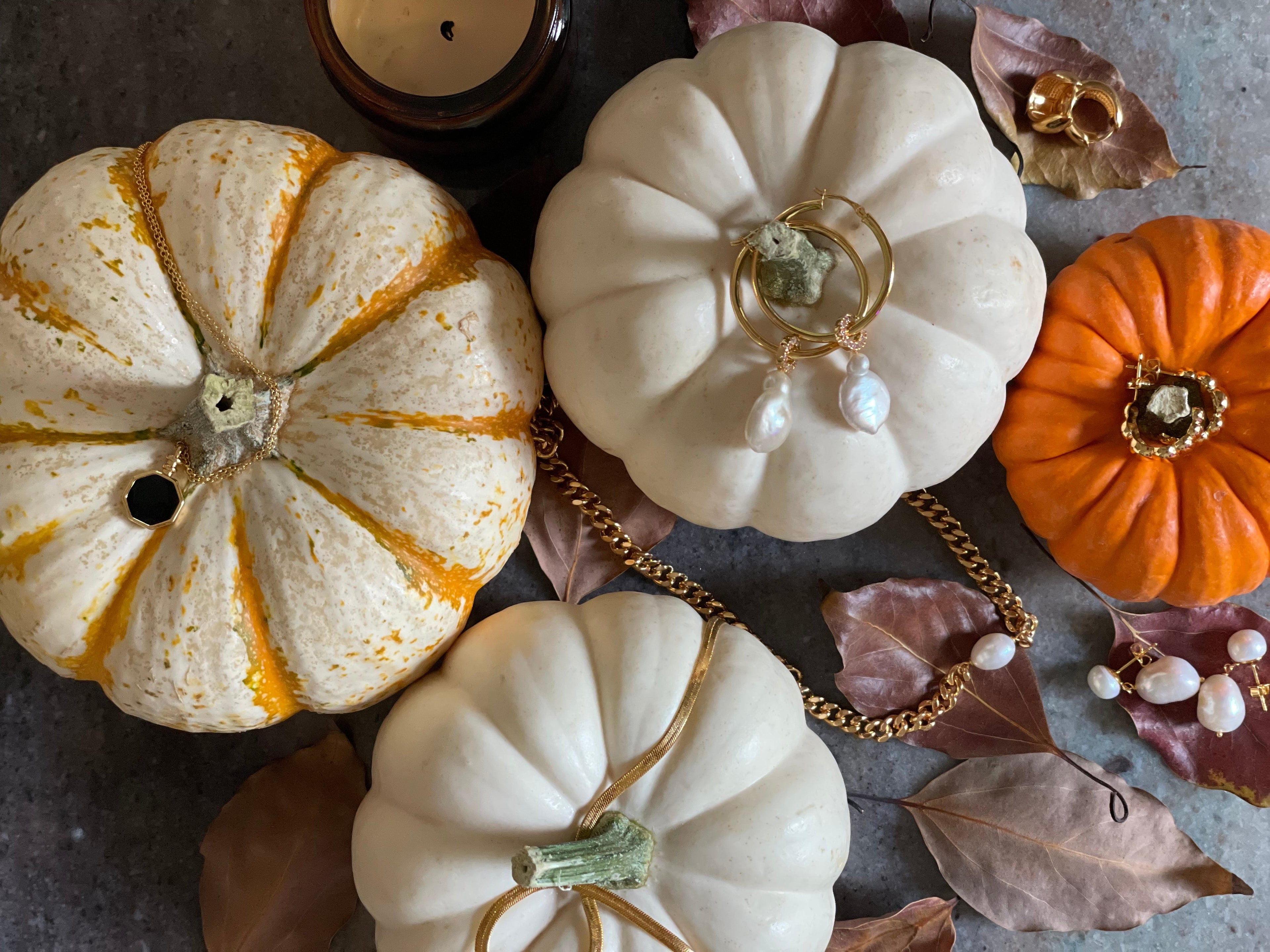 Decorative pumpkins with jewelry on a textured surface with leaves and candles.