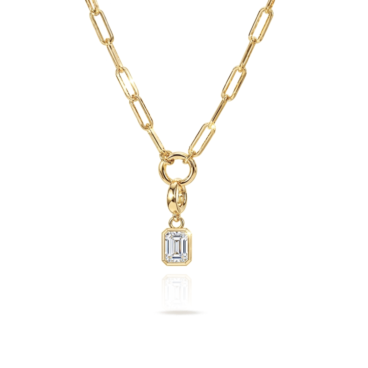 A gold paperclip chain necklace with a small rectangular emerald-cut clear gemstone pendant, shown on a clean white background with a soft reflection below.