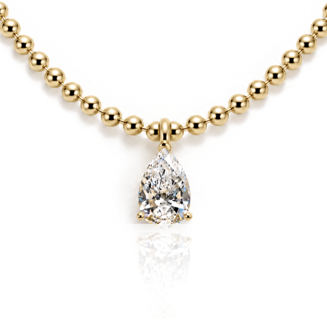 A gold beaded necklace with a pear-cut diamond pendant, displayed on a clean white background with a soft reflection below.