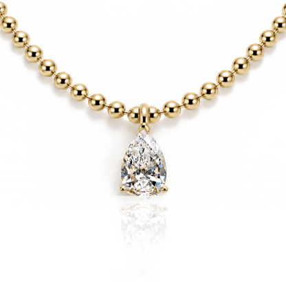 A gold beaded necklace with a pear-cut diamond pendant, displayed on a clean white background with a soft reflection below.