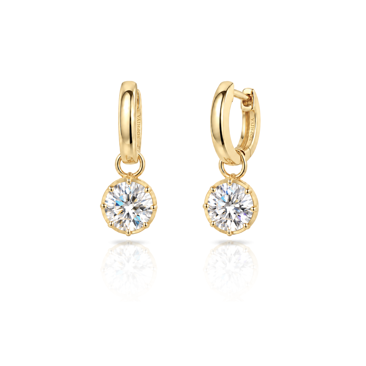 A pair of gold huggie hoop earrings with round bezel-set clear gemstones, displayed on a clean white background with a soft reflection below.