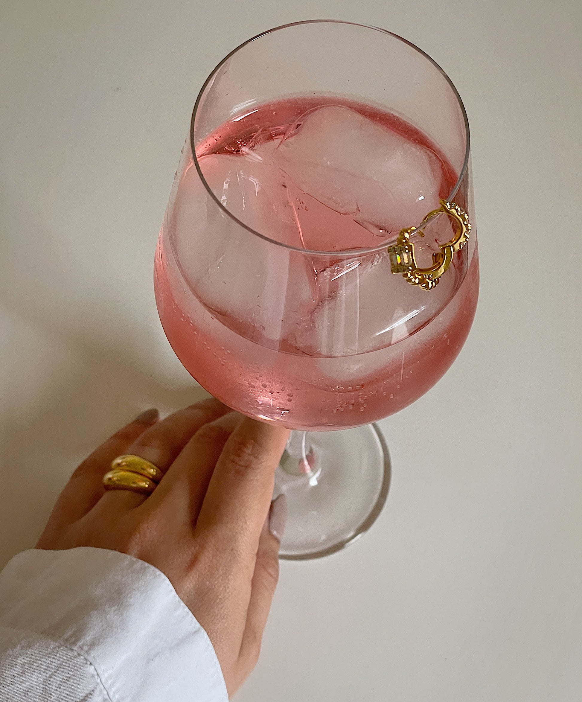 Camille Huggie Earrings featuring CZ and summer mocktails, held by feminine hand with stacked gold Dylan rings