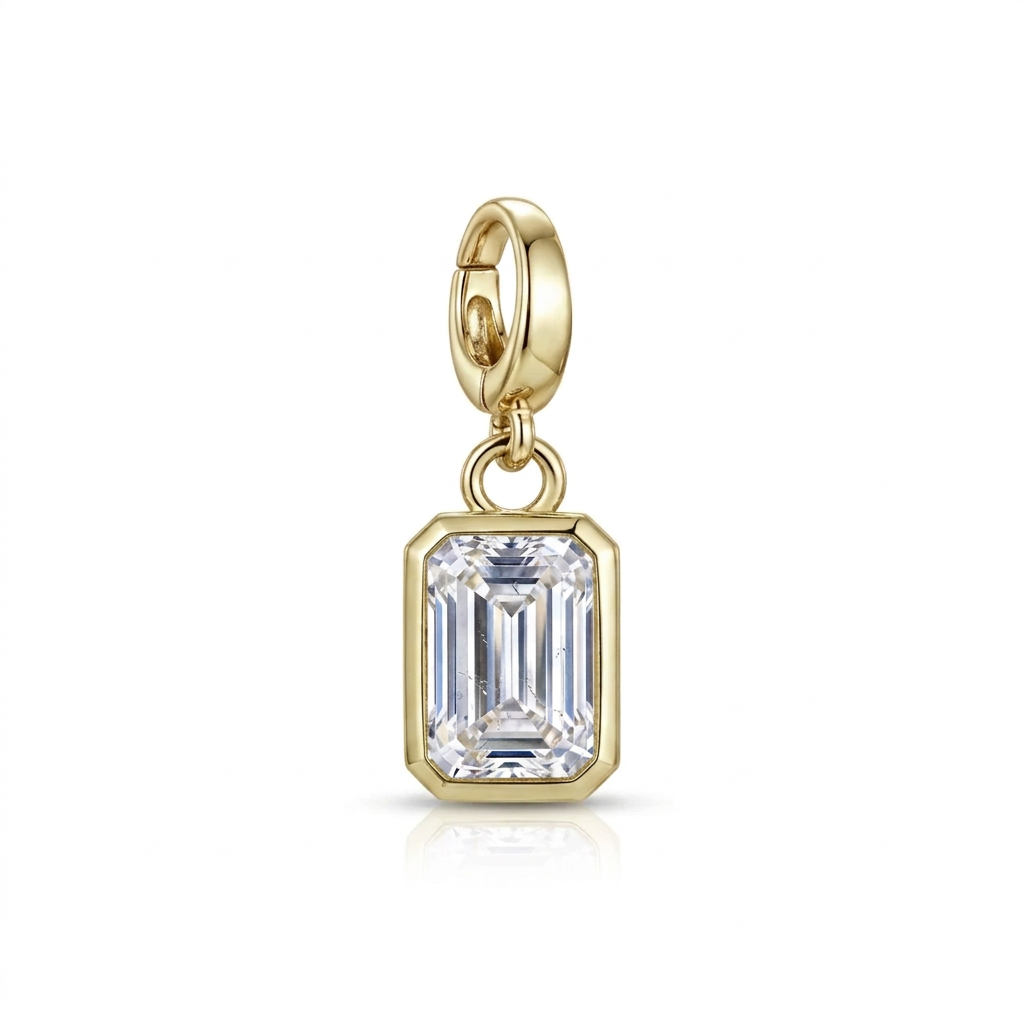 A gold charm featuring an emerald-cut clear gemstone in a gold bezel setting, suspended from a gold lobster clasp, shown on a white background with a soft reflection.