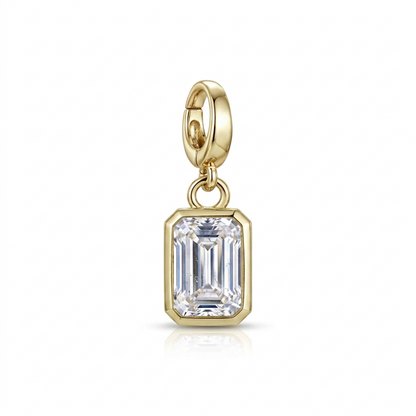 A gold charm featuring an emerald-cut clear gemstone in a gold bezel setting, suspended from a gold lobster clasp, shown on a white background with a soft reflection.