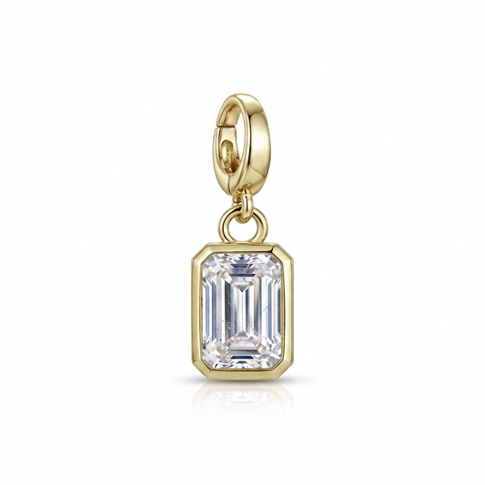 A gold charm featuring an emerald-cut clear gemstone in a gold bezel setting, suspended from a gold lobster clasp, shown on a white background with a soft reflection.