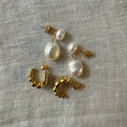 Natural linen elements bring out semi round pearl textures on Charlotte pearl earrings laying next to 18k gold ridged Celine earrings