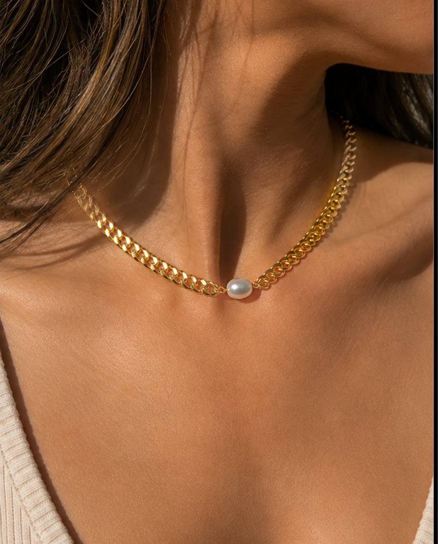 A close-up of a model's neck and chest wearing a gold chain choker necklace with a single white pearl pendant.