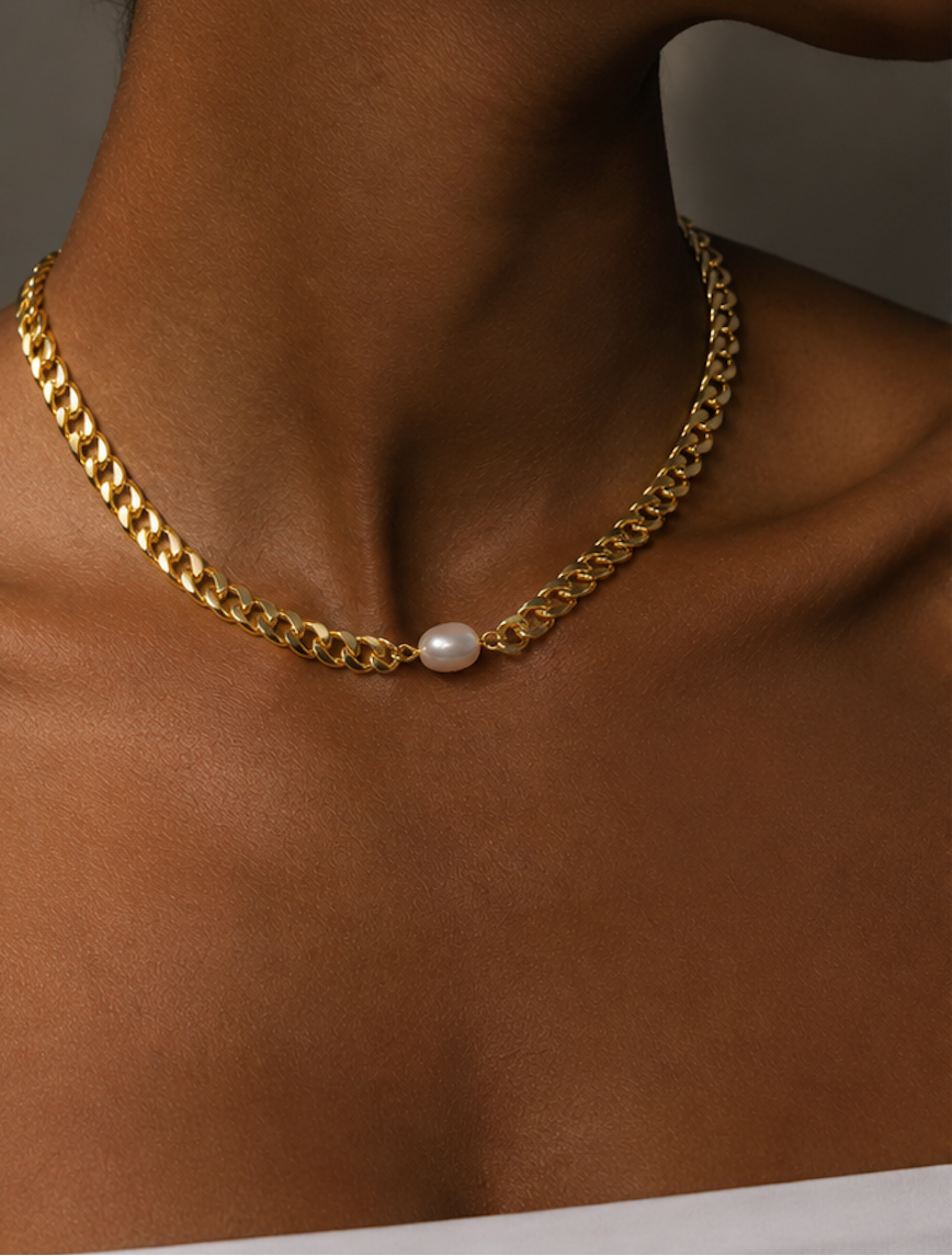 A close-up of a model's neck and collarbone wearing a gold chain necklace with a single white pearl pendant.
