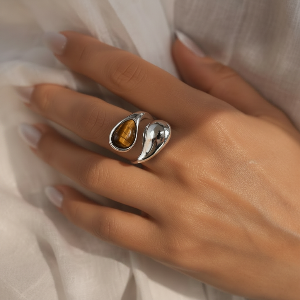 A close-up of a hand wearing a polished silver ring with an organic, flowing abstract shape, resting on white textured fabric.