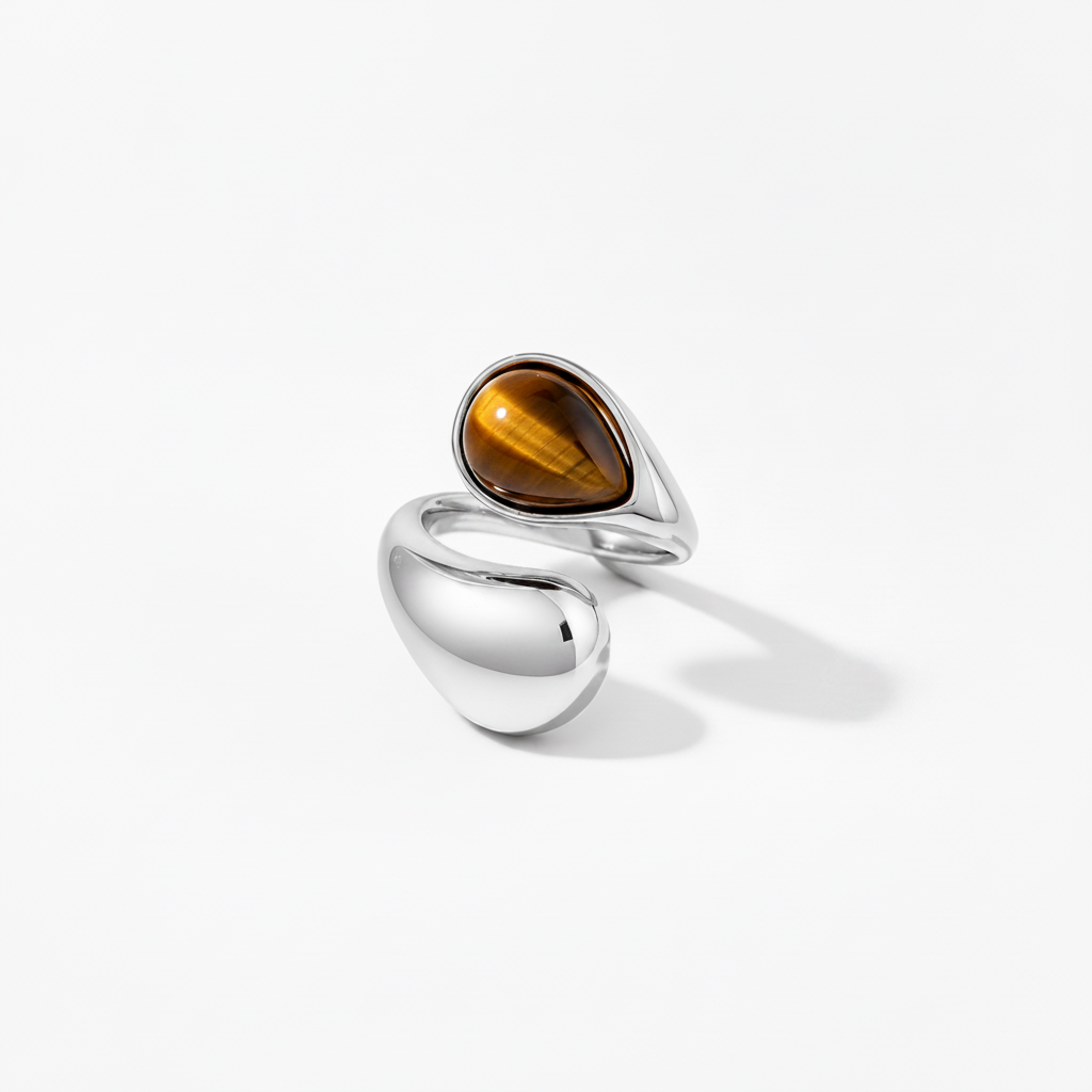 A modern sterling silver ring featuring a teardrop-shaped brown tiger's eye stone and a large smooth polished bead-shaped silver accent, set against a clean white background.