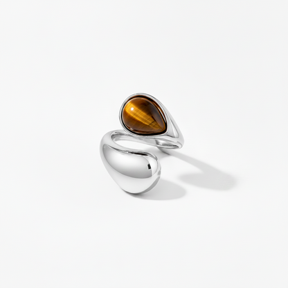 A modern sterling silver ring featuring a teardrop-shaped brown tiger's eye stone and a large smooth polished bead-shaped silver accent, set against a clean white background.