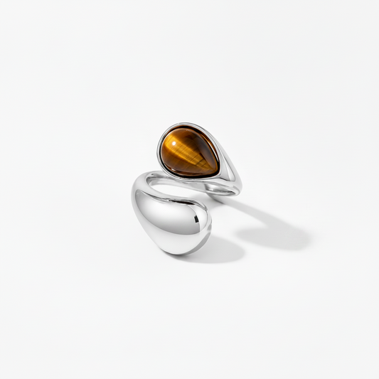 A modern sterling silver ring featuring a teardrop-shaped brown tiger's eye stone and a large smooth polished bead-shaped silver accent, set against a clean white background.