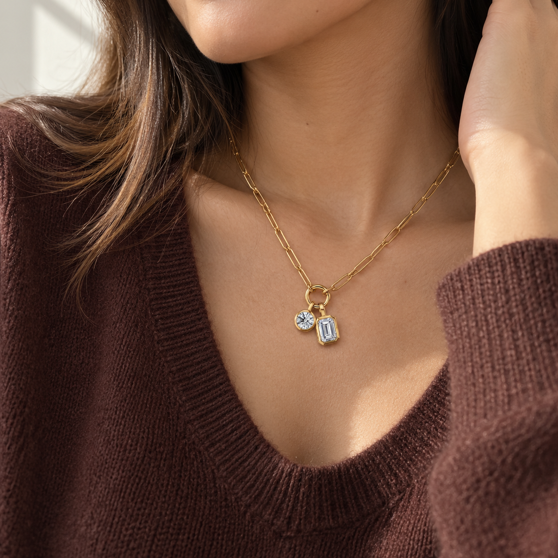 A close-up lifestyle shot of a woman wearing a delicate gold chain necklace with two small clear gemstone charms, paired with a brown knit sweater.