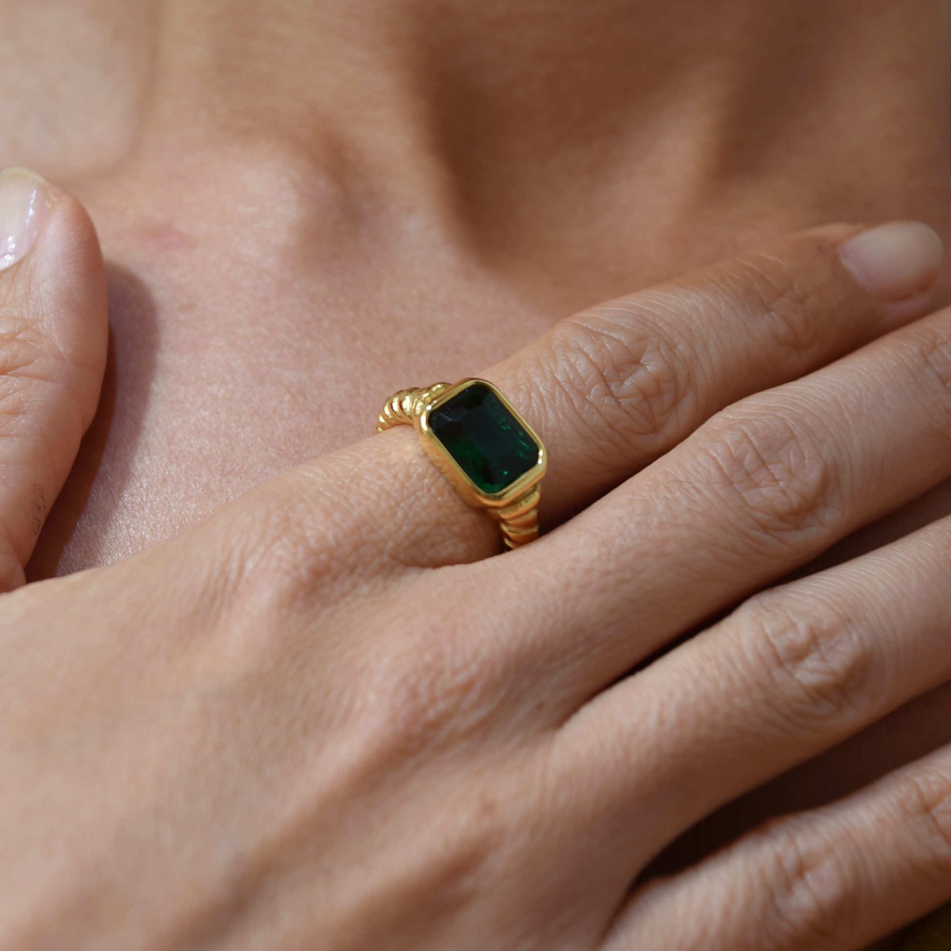 Gold ring with a green gemstone on a person's finger